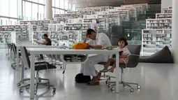 Pengunjung pria duduk bersama seorang balita di dalam Perpustakaan Nasional Qatar di ibu kota Doha pada 19 Mei 2019. Dibuka pada 16 April 2018, pembangunan perpustakaan ini diperkirakan menelan biaya sekitar US$300 juta (sekitar Rp4,2 miliar). (KARIM JAAFAR / AFP)