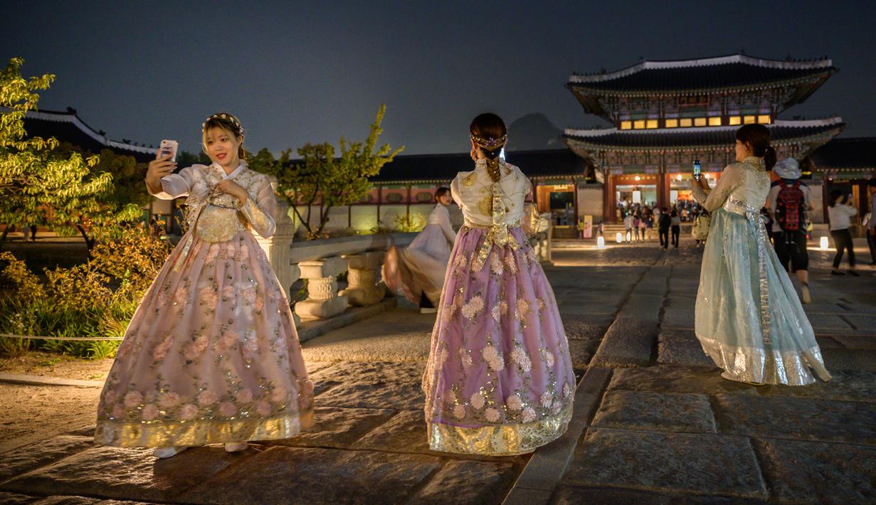 Pengunjung mengenakan gaun tradisional Korea, hanbok sambil berpose saat kunjungan malam ke Istana Gyeongbokgung di Seoul, 4 Oktober 2019. Kunjungan malam tersedia pada minggu ketiga dan keempat setiap bulan mulai dari 26 April sampai 31 Oktober, kecuali pada bulan Agustus. (Photo by Ed JONES / AFP)