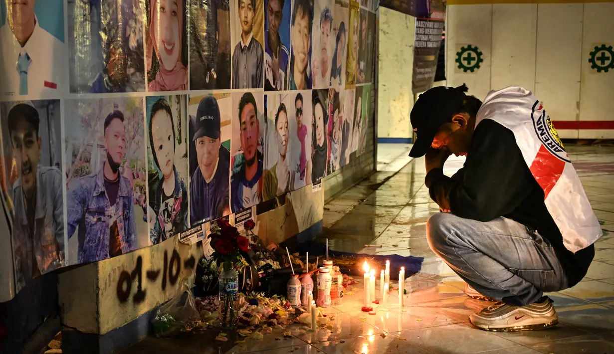 Seorang pria berduka di depan tugu peringatan dengan potret para korban di dinding sebelum doa pada peringatan satu tahun tragedi terburuk dalam sejarah sepak bola Indonesia di stadion Kanjuruhan Malang, Jawa Timur, pada 1 Oktober 2023. (Juni Kriswanto/AFP)