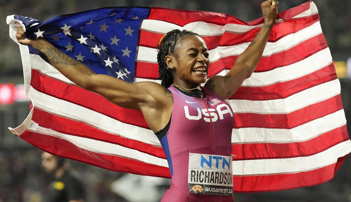 Pelari Amerika Serikat, Sha’Carri Richardson membentangkan bendera negaranya saat melakukan selebrasi memenangkan final 100 meter putri Kejuaraan Dunia Atletik 2023 di National Athletics Centre, Budapest, Hungaria, pada 22 Augustus 2023. (AP Photo/Ashley Landis)