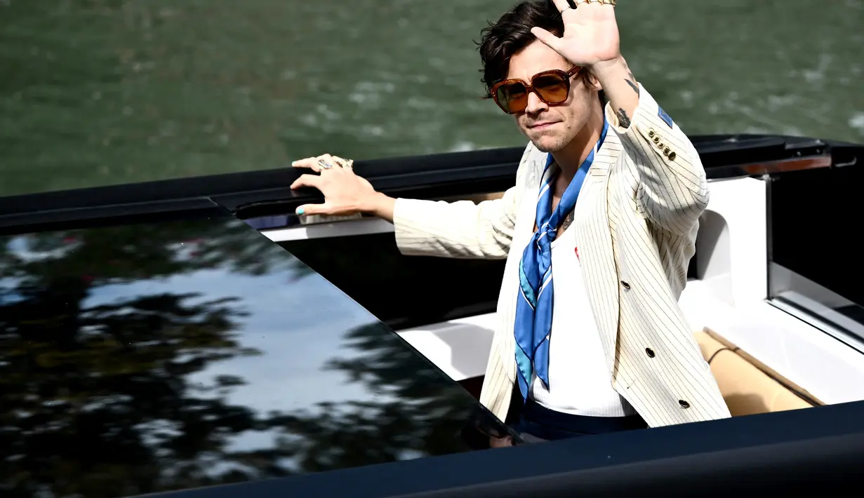 Harry Styles melambaikan tangan saat ia tiba di dermaga Hotel Excelsior selama Venice Film Festival 2022 ke-79 di Venesia, Italia (5/9/2022). Pria 29 tahun itu berperan sebagai Jack Dalam film “Don’t Worry Darling,”. (AFP/Marco Bertorello)