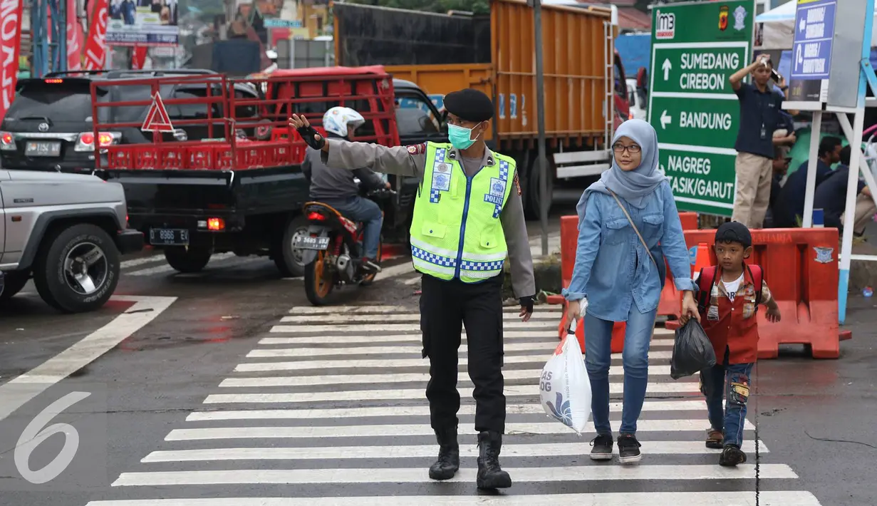 Petugas kepolisian membantu warga menyeberang jalan di Perempatan Cileunyi, Jawa Barat, Jumat (1/7). Mulai banyaknya kendaraan pemudik membuat petugas kepolisian membantu pejalan kaki yang ingin menyeberang. (Liputan6.com/Immanuel Antonius) 