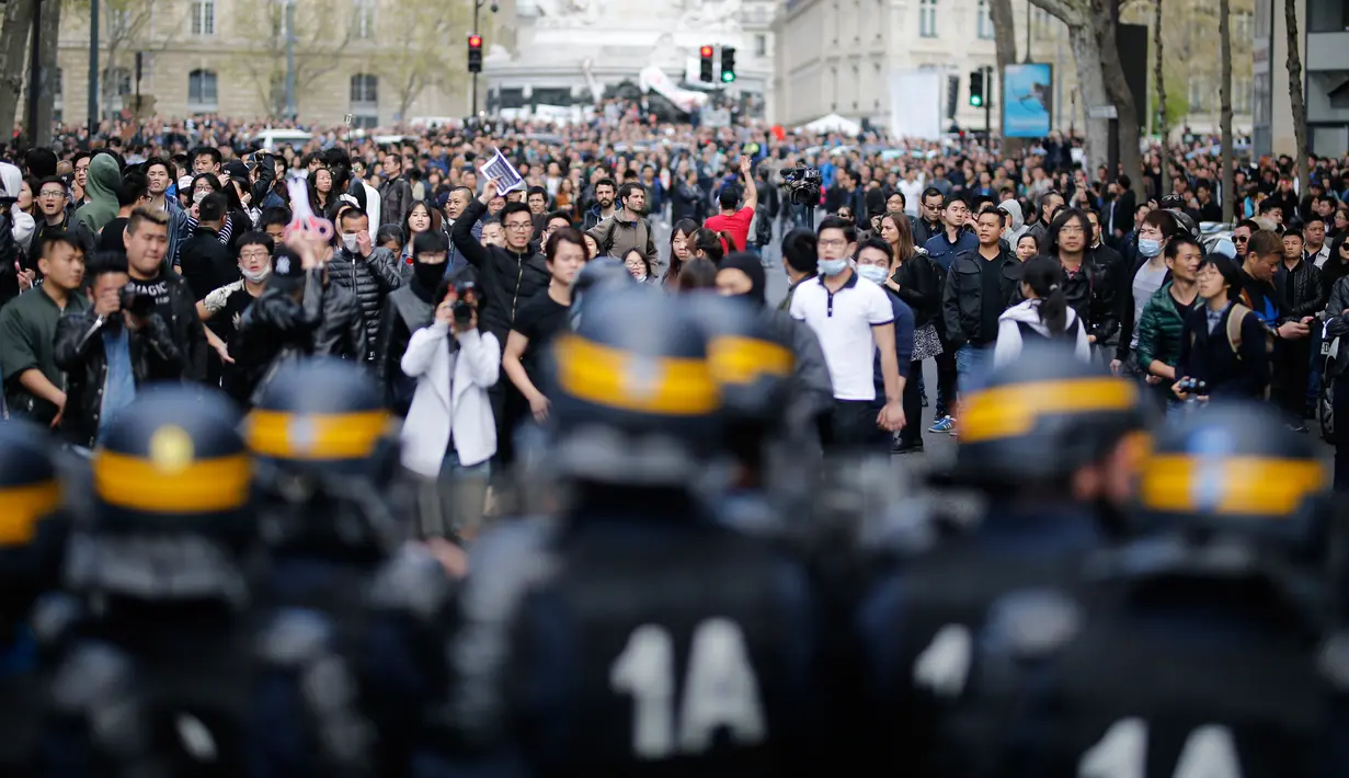 Polisi anti huru hara berjaga didepan para demonstran di Place de la Republique, di Paris, Prancis (2/4). Setidaknya 6.000 orang yang tergabung dalam komunitas etnis China di Prancis turun ke jalanan kota Paris menggelar aksi protes. (AFP/Benjamin Cremel)
