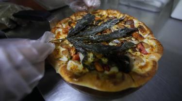Seorang pekerja menghias pizza dengan daun ganja goreng di sebuah restoran di Bangkok, pada 24 November 2021. The Pizza Company, jaringan makanan cepat saji utama Thailand memperkenalkan makanan andalannya bulan ini, yakni pizza ganja berjuluk ‘Crazy Happy Pizza’. (AP Photo/Sakchai Lalit)