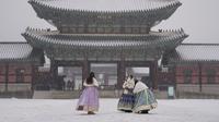 Pengunjung yang mengenakan masker untuk membantu mengekang penyebaran virus corona berfoto di tengah salju di Istana Gyeongbok, salah satu landmark terkenal Korea Selatan, di Seoul, Korea Selatan, Rabu (19/1/2022). (AP Photo/Lee Jin-man)