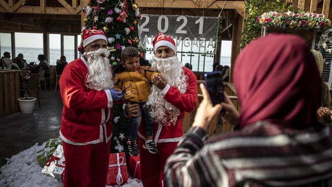 Pramusaji Palestina berpakaian Sinterklas menggendong seorang anak untuk berfoto di sebuah restoran di pantai di Kota Gaza, Minggu (13/12/2020). REstoran tersebut didandani dengan tema Natal, pelayanannya pun berpakaian seperti Sinterklas. (AP Photo/Khalil Hamra)