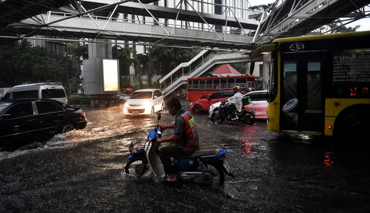 Pengendara berkendara melalui jalan yang banjir saat hujan deras di Bangkok (23/9/2020). (AFP/Mladen Antonov)