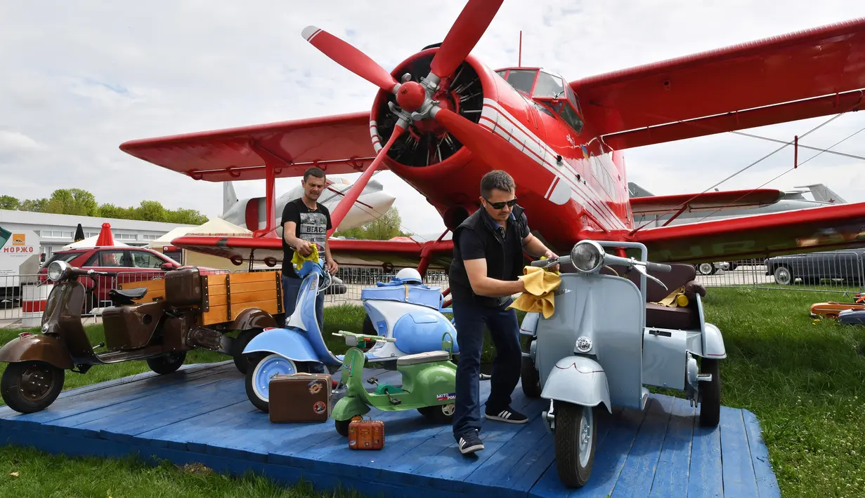 Para peserta membersihkan skuter di sebelah airplaine selama hari pembukaan festival mobil retro OldCarLand di Kiev (27/4). Pameran kendaraan jadul ini digelar dari 27 April hingga Mei, 1, 2018. (AFP Photo/Sergei Supinsky)