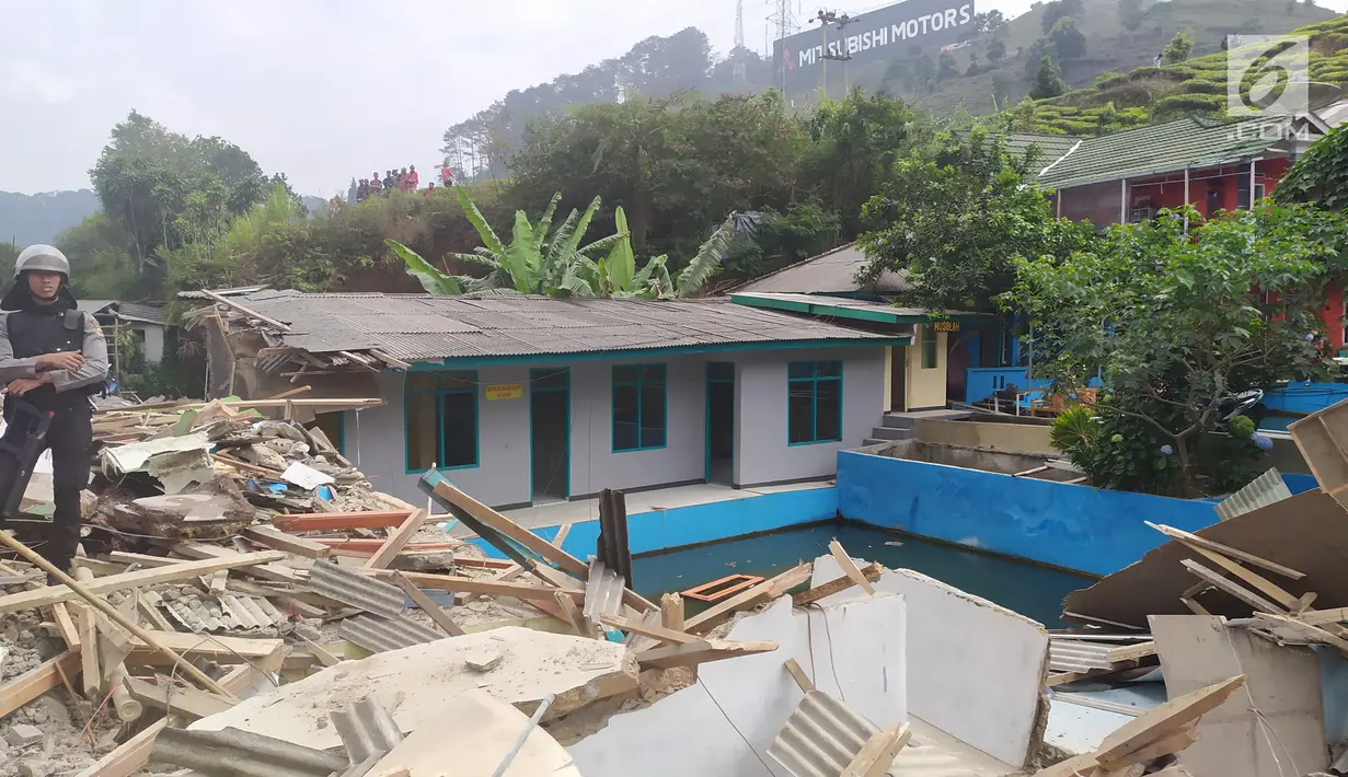Personel Polres Bogor berdiri di atas sisa reruntuhan bangunan yang dibongkar di Kampung Naringgul, Kabupaten Bogor, Kamis (29/8/2019). Sebanyak 500 petugas gabungan dari Satpol PP, TNI dan Polri serta dua unit alat berat diterjunkan dalam pembongkaran tersebut. (Liputan6.com/Alby Azka)