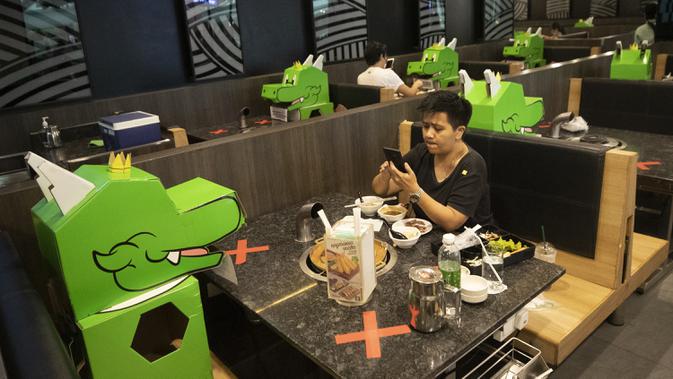 Pelanggan duduk berhadapan dengan boneka kartun naga yang digunakan restoran untuk menjaga jarak fisik di Bangkok, Thailand, Senin (18/5/2020). Pemerintah Thailand mengizinkan pusat perbelanjaan dan bisnis kembali dibuka setelah sebelumnya ditutup karena pandemi COVID-19. (AP Photo/Sakchai Lalit)