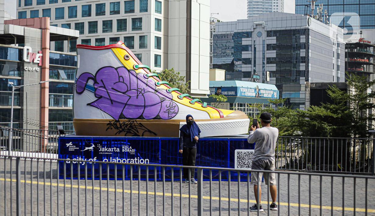 Warga berfoto di depan Tugu Sepatu, Sudirman, Jakarta, Minggu (19/9/2021). Tugu Sepatu menjadi sasaran pencoretan dengan semprotan aerosol oleh orang tak dikenal sehari usai diresmikan pada 17 September 2021. (Liputan6.com/Faizal Fanani)