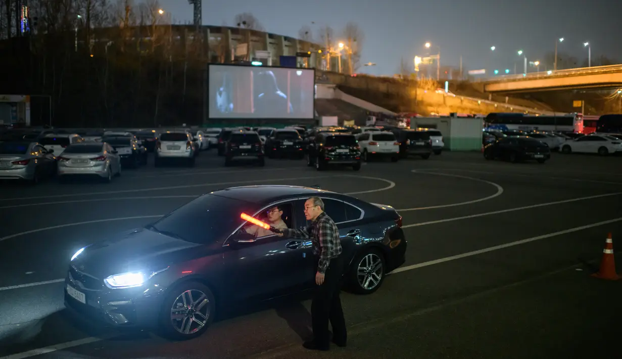 Petugas mengarahkan pelanggan menuju layar film di sebuah bioskop kendara atau drive-in cinema di Seoul, Korea Selatan. Jenis bioskop ini menjadi pilihan yang lebih bagi warga Seoul untuk menikmati film di tengah pandemi virus corona Covid-19 yang mewabah di sejumlah negara. (Ed JONES/AFP)