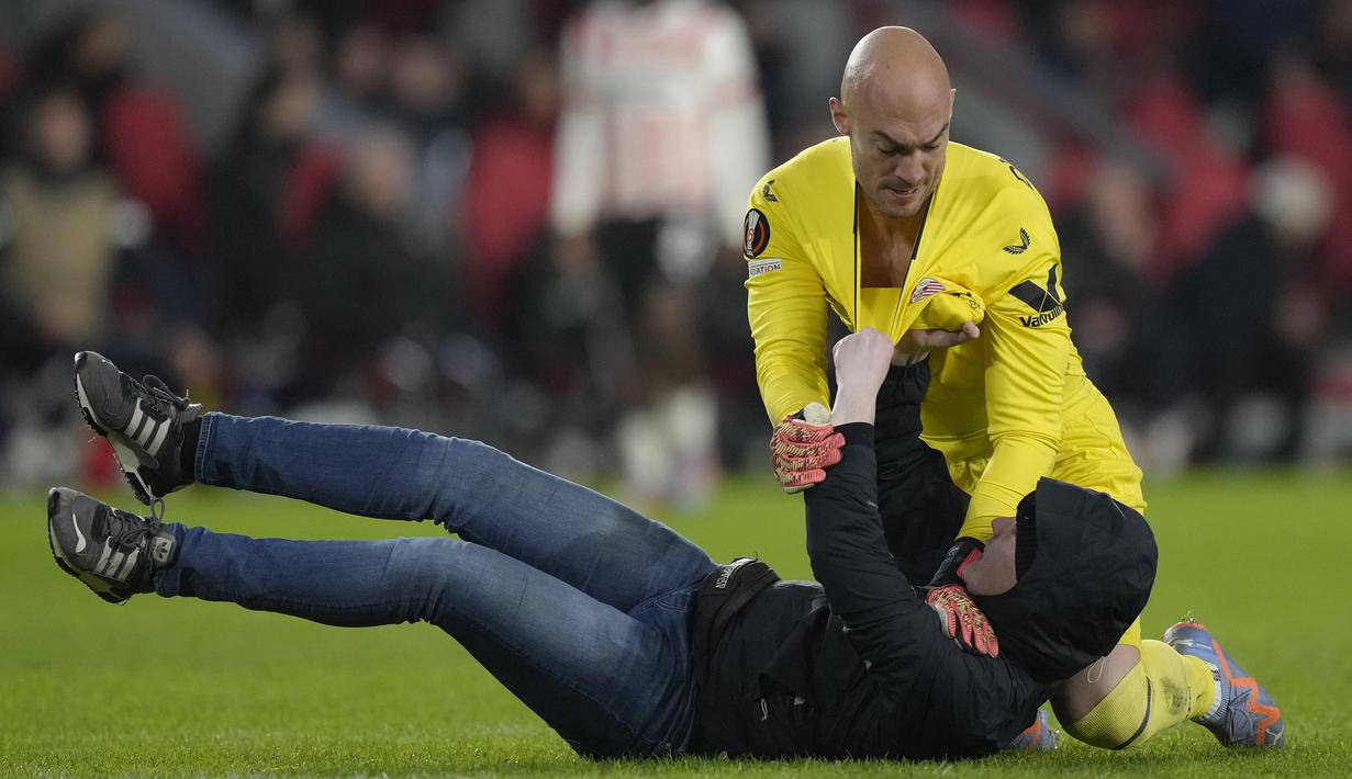 <p>Kiper Sevilla, Marko Dmitrovic berhasil melumpuhkan seorang suporter fanatik PSV yang menyerangnya dalam laga leg kedua babak playoff fase gugur Liga Europa 2022/2023 di Philips Stadium, Eindhoven, Jumat (24/2/2023). (AP Photo/Peter Dejong)</p>
