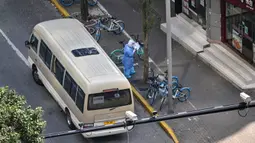 Seorang petugas kesehatan yang mengenakan alat pelindung diri berdiri sebelah bus Changning Covid Controls di depan pintu masuk ke lingkungan saat lockdown tahap kedua akibat COVID-19 di Distrik Jing'an, Shanghai, China, Rabu (6/4/2022). (Hector RETAMAL/AFP)