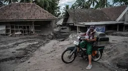 Seorang pria mengendarai sepeda melewati rumah yang rusak akibat erupsi Gunung Semeru di Desa Sumber Wuluh, Lumajang, Jawa Timur, Senin (6/12/2021). Desa Sumber Wuluh luluh lantak diterjang erupsi Semeru mengakibatkan puluhan rumah rusak dan ratusan warga mengungsi. (Juni Kriswanto/AFP)