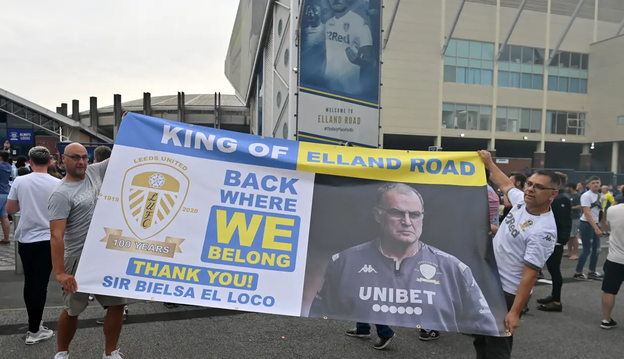 Pendukung Leeds United mengangkat spanduk besar saat mereka berkumpul di luar tanah Elland Road mereka untuk merayakan kembalinya klub ke Liga Premier setelah  16 tahun, di Leeds, Inggris utara (17/7/2020). (AFP/Paul Ellis)