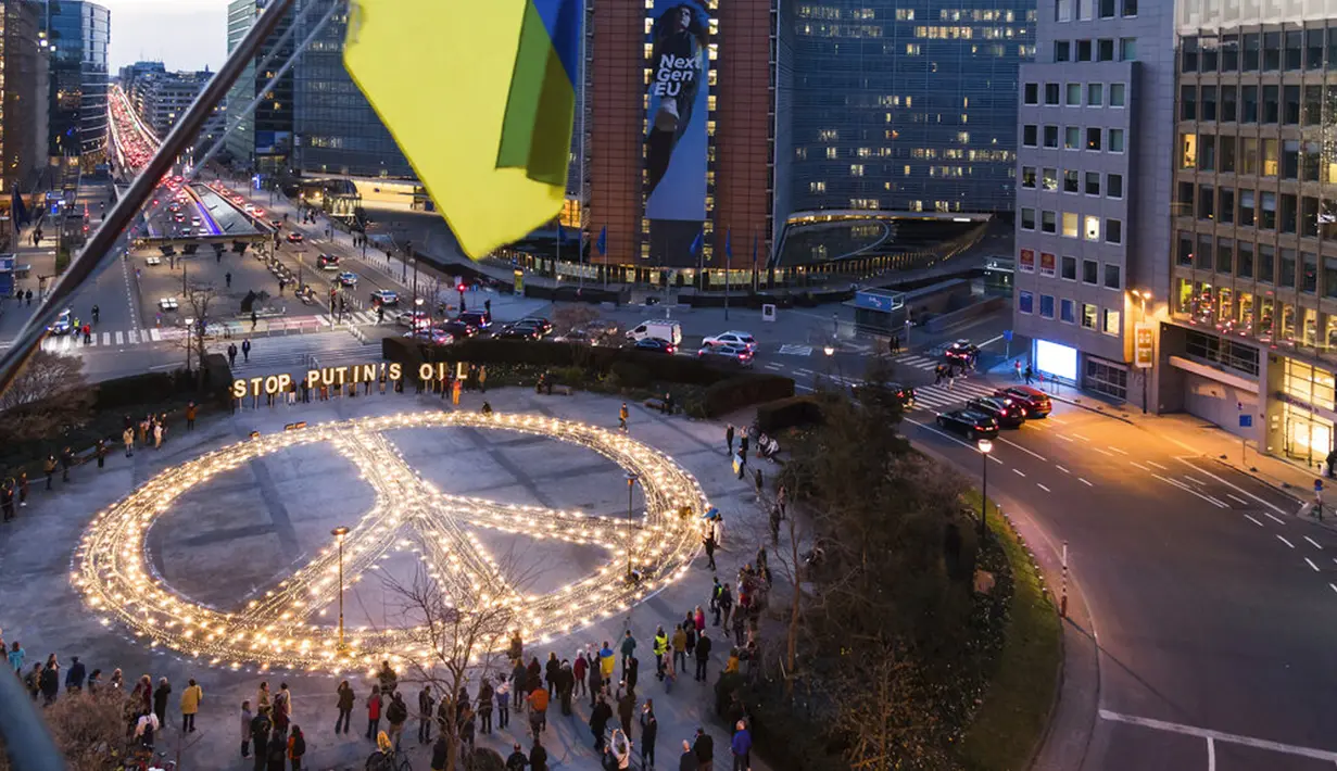 Bendera Ukraina berkibar ditiup angin saat tanda perdamaian raksasa dipasang para demonstran jelang KTT Uni Eropa dan NATO di Brussels, Belgia, 22 Maret 2022. Pengunjuk rasa meminta para pemimpin Uni Eropa memberlakukan larangan penuh terhadap bahan bakar Rusia. (AP Photo/Geert Vanden Wijngaert)