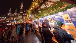 Wisawatan mengunjungi stand yang ada di pasar Natal di luar City Hall, Wina pada 26 November 2018. Di Pasar Natal ini, para pengunjung bisa menikmati jajanan khas hingga pernak-pernik kerajinan tangan asli Austria. (JOE KLAMAR / AFP)