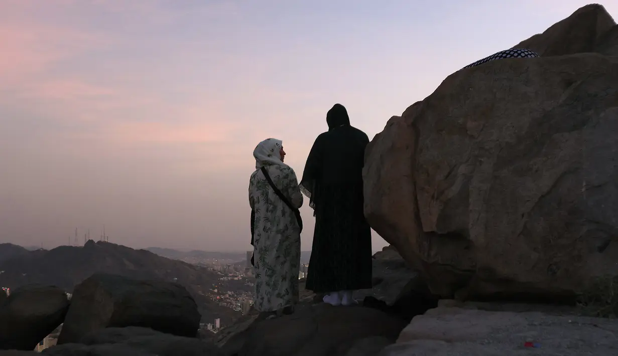 Peziarah muslim berdiri di Jabal al-Noor atau Gunung Cahaya yang menghadap ke Kota Suci Mekkah, Arab Saudi, 5 Juli 2022. Satu juta orang, termasuk 850 ribu dari luar negeri, diizinkan untuk berpartisipasi dalam haji tahun ini setelah dua tahun terakhir jumlahnya dikurangi secara drastis karena pandemi virus corona COVID-19. (Christina ASSI/AFP)