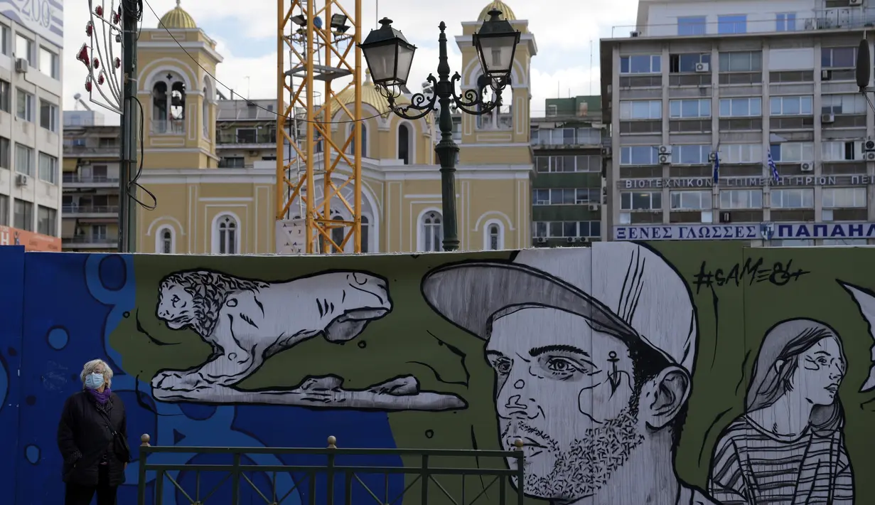 Seorang wanita mengenakan masker berdiri di dekat mural di pelabuhan Piraeus, Athena, Senin (13/12/2021). Yunani meningkatkan kampanye vaksinasi menjelang liburan Natal saat negara itu bergulat dengan lonjakan infeksi yang membawa angka kematian COVID-19 mendekati rekor. (AP/Thanassis Stavrakis)