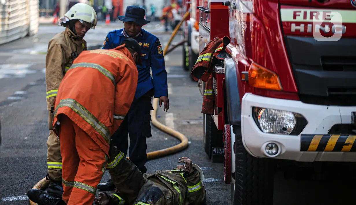 Petugas pemadam kebakaran membantu rekannya setelah melakukan pendingan di Kejaksaan Agung RI yang terbakar, Minggu (23/8/2020). Kebakaran di gedung Kejaksaan Agung pada Sabtu (22/8) malam akhirnya padam dan kini bangunan tersebut menyisakan bagian hitam legam. (Liputan6.com/Faizal Fanani)