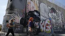 Wisatawan berjalan melewati grafiti yang menggambarkan Presiden AS Donald Trump di tembok pemisah Israel - Palestina di kota Bethlehem (4/8). Tembok ini memisahkan antara Israel dan Palestina. (AFP Photo/Musa Al Shaer)