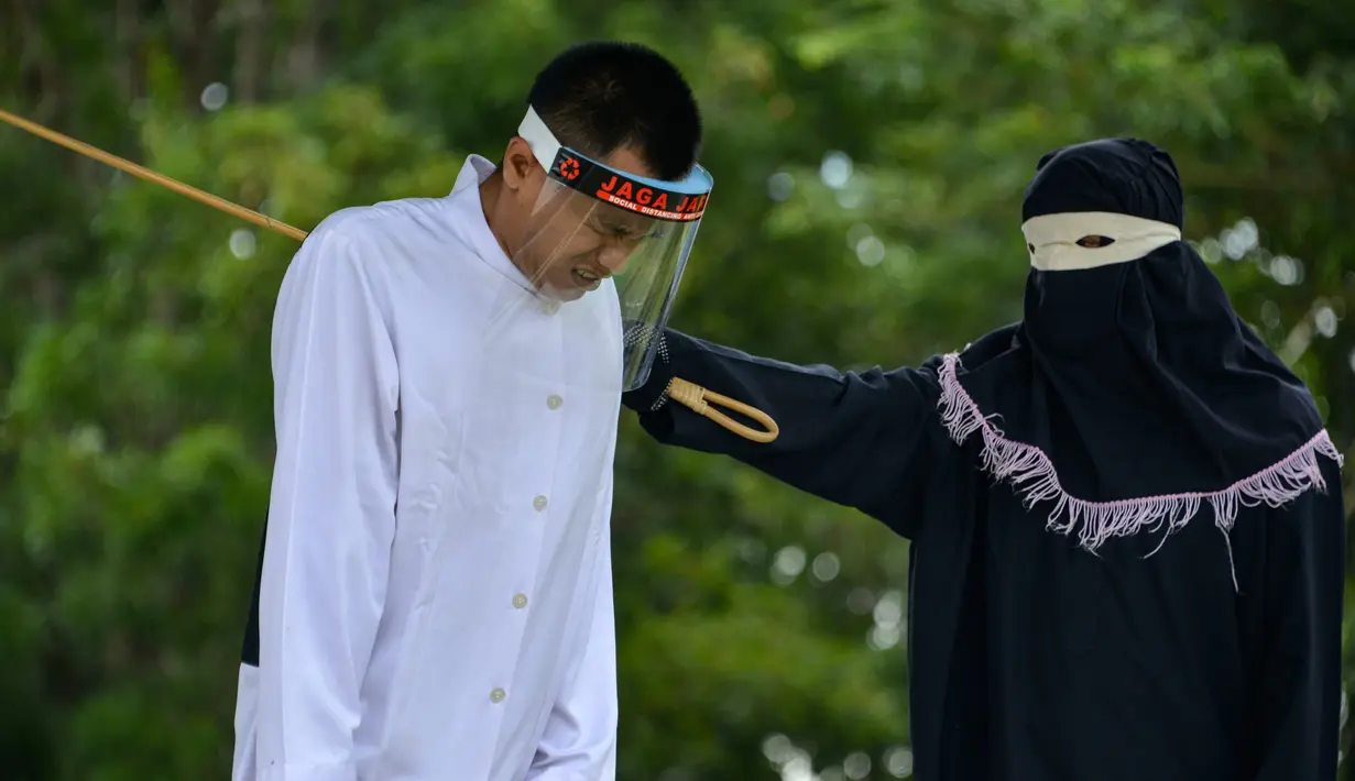 Salah seorang pasangan terpidana kasus zina (kiri) menjalani hukuman cambuk di Masjid Al Munawarah, Kota Jantho, Aceh Besar, Jumat (4/9/2020). Pasangan terpidana yang terbukti melanggar Syariat Islam dalam kasus zina itu masing masing menjalani sebanyak 100 cambuk. (CHAIDEER MAHYUDDIN/AFP)