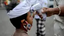 Seorang anak laki-laki melakukan pengecekan suhu tubuhnya sebelum memasuki pura untuk merayakan festival keagamaan Galungan di Pura Jagat Natha di Denpasar, di pulau Bali (16/9/2020). (AFP Photo/Sonny Tumbelaka)
