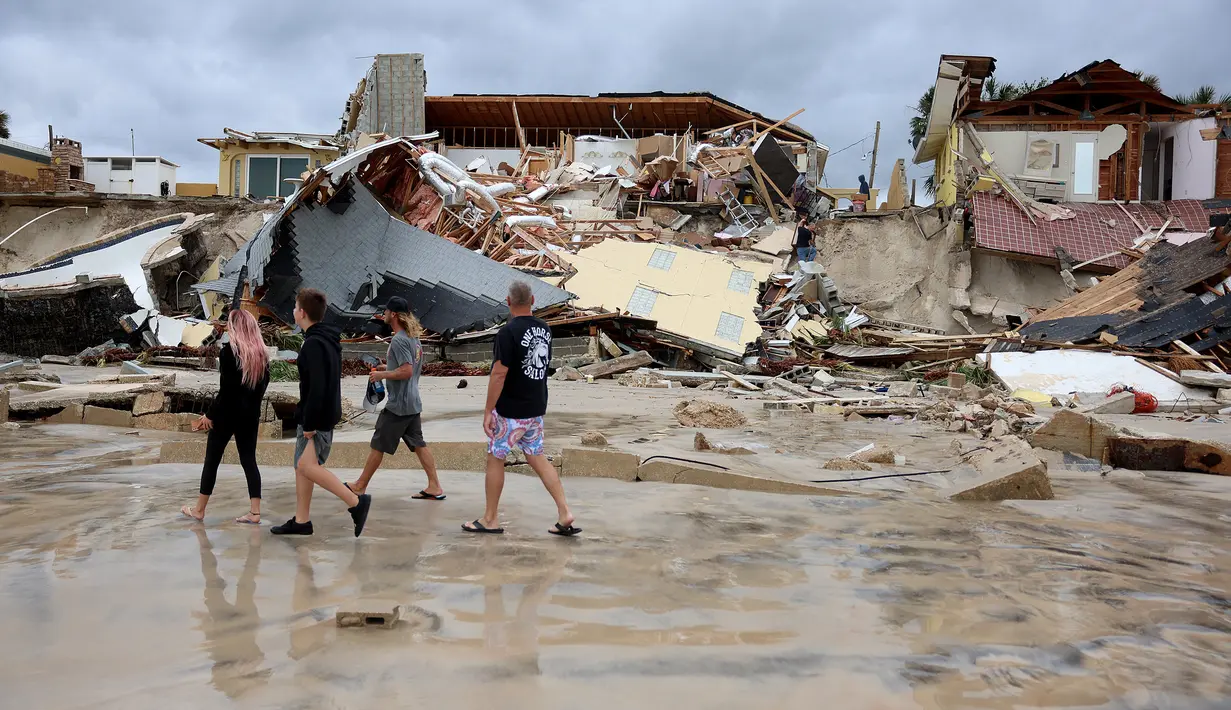 Penduduk melewati rumah-rumah yang sebagian roboh ke pantai setelah Badai Nicole mendarat di Pantai Daytona, Florida (10/11/2022). Badai Nicoler datang ke darat sebagai badai Kategori 1 sebelum melemah menjadi badai tropis saat bergerak melintasi negara bagian. (Joe Raedle/Getty Images/AFP)
