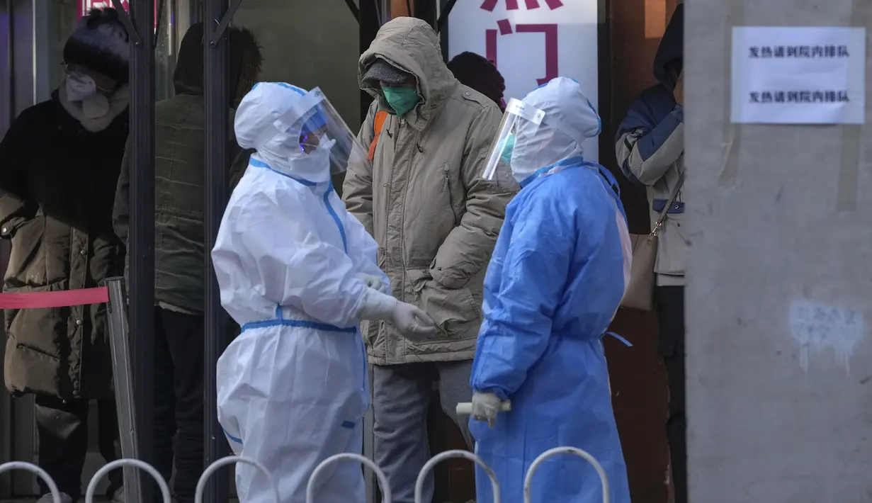 Petugas medis berbaju pelindung saling mengobrol saat warga menunggu masuk ke klinik demam sebuah rumah sakit di Beijing, Selasa (13/12/2022). Beberapa universitas di China mengatakan akan mengizinkan mahasiswanya menyelesaikan semester dari rumah dengan harapan mengurangi potensi wabah COVID-19 yang lebih besar selama kesibukan perjalanan Tahun Baru Imlek di bulan Januari mendatang. (AP Photo/Andy Wong)