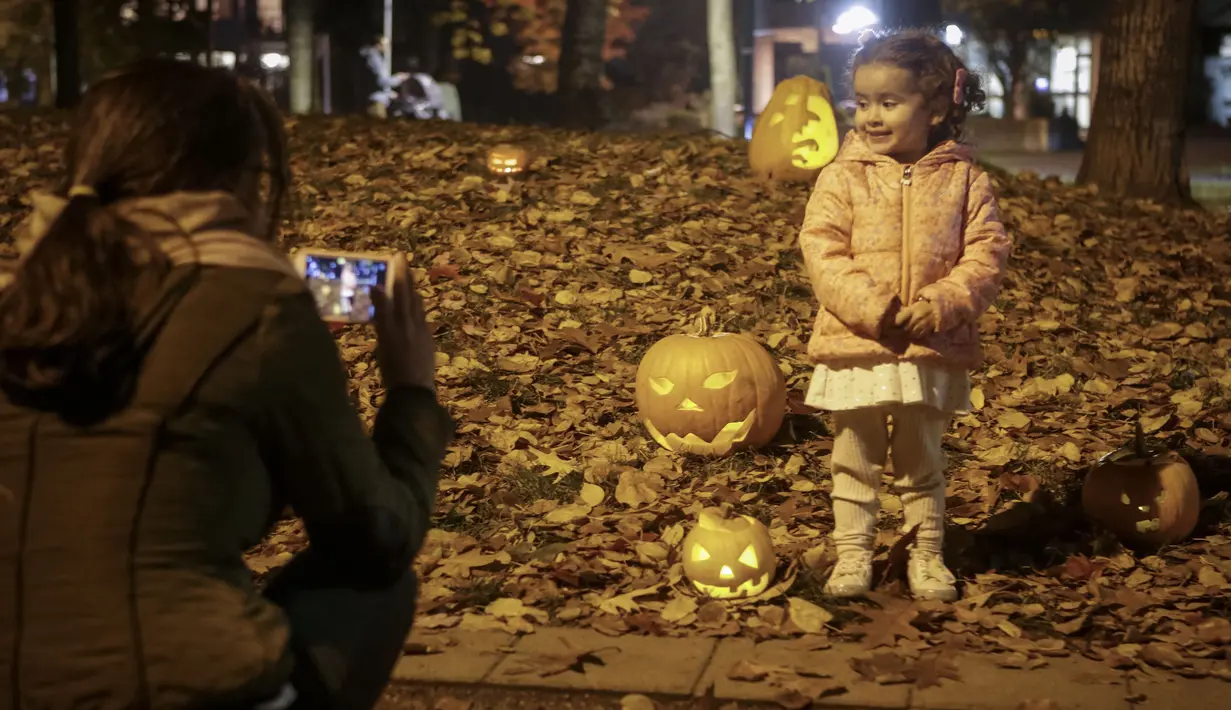 Seorang anak kecil berfoto dengan labu yang diukir dalam Parade Labu tahunan ketiga di Nelson Park di Vancouver, British Columbia, Kanada, pada 1 November 2020. (Xinhua/Liang Sen)