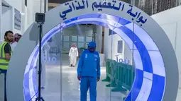Pekerja melewati gerbang sterilisasi mandiri yang didirikan di pintu masuk Ka'bah dan Masjidil Haram sebagai langkah pencegahan di tengah pandemi COVID-19 di Mekkah pada 8 Mei 2020. Gerbang ini dilengkapi teknologi canggih berupa kamera thermal untuk mendeteksi suhu dari jarak 6 meter. (STR / AFP)