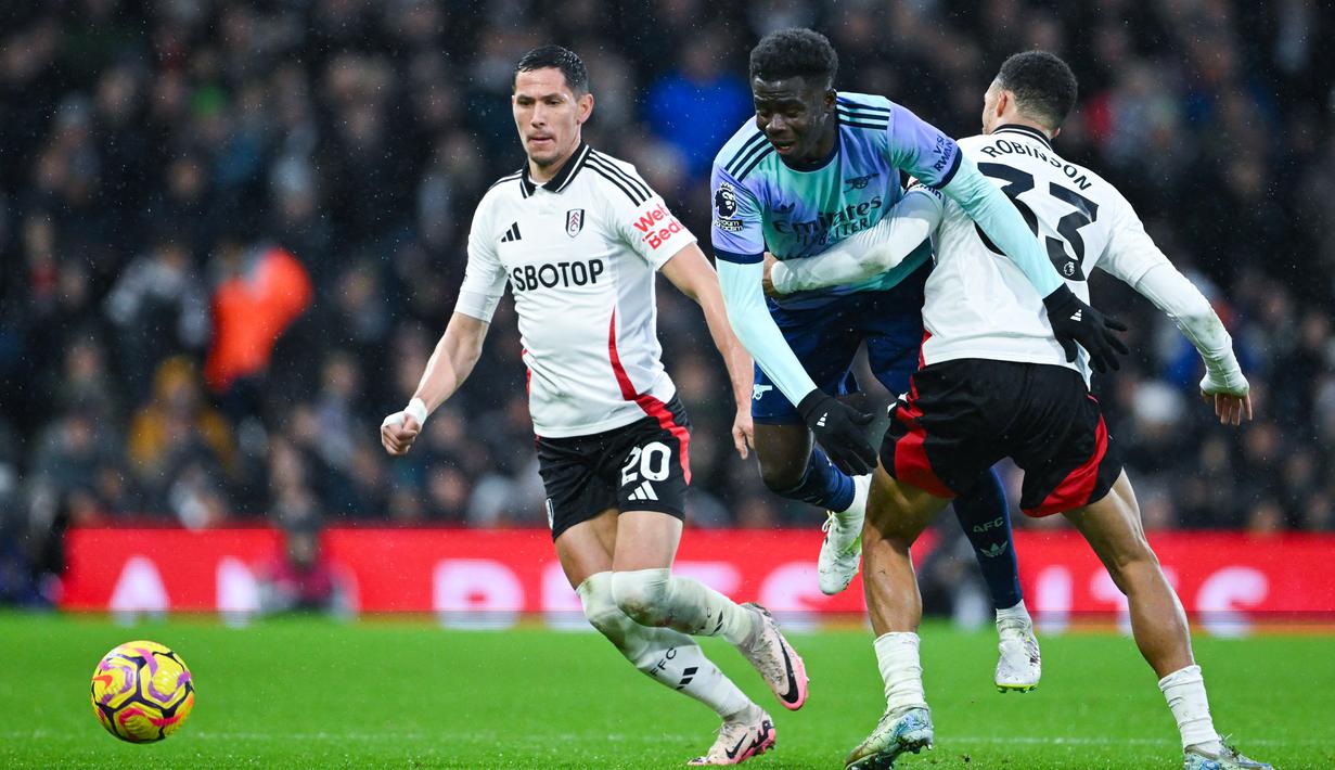 Pemain Fulham, Antonee Robinson, berusaha mengadang pergerakan pemain Arsenal, Bukayo Saka dalam lanjutan Liga Inggris di Craven Cottage, Minggu (9/12/2024). (AFP/Justin Tallis)