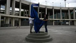 Orang-orang membuka tanda jalan bertuliskan "Avenue King Pele" di luar stadion Maracana di Rio de Janeiro, Brasil pada 4 Januari 2023. Balai Kota Rio de Janeiro secara resmi menamai jalan yang mengelilingi stadion Maracana Avenue Rei Pele (King Pele). (MAURO PIMENTEL/AFP)