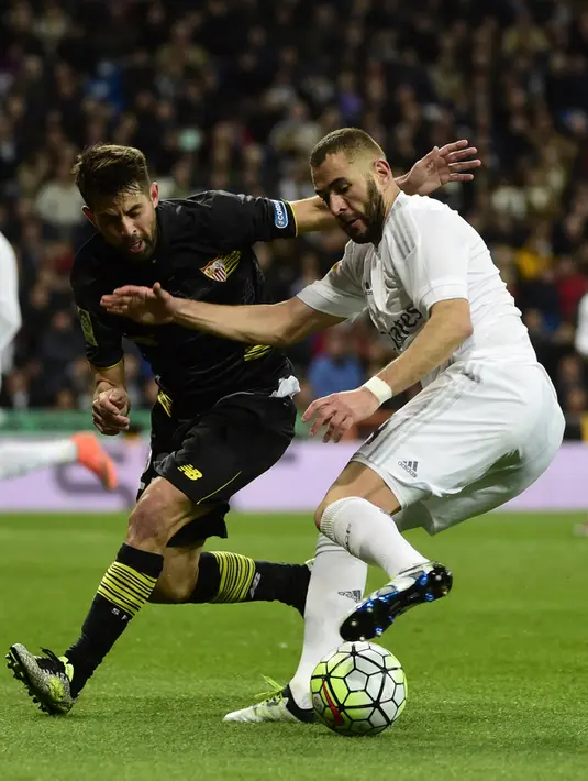 Penyerang Real Madrid, Karim Benzema (kanan) berusaha melewati bek Sevilla, Coke pada Liga Spanyol di Stadion Santiago Bernabeu (21/3). Real Madrid menang besar atas Sevilla dengan skor 4-0. (AFP/PIERRE-PHILIPPE Marcou)