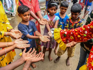 Relawan pekerja sosial Ashok Kurmi, berpakaian seperti badut, menyemprotkan hand sanitiser kepada anak-anak di daerah kumuh Mumbai pada 2 Juni 2021. Kurmi turun tangan memerangi Corona COVID-19 di daerah kumuh Mumbai menggunakan aksesori yang tidak biasa, yaitu kostum badut. (INDRANIL MUKHERJEE/AFP)