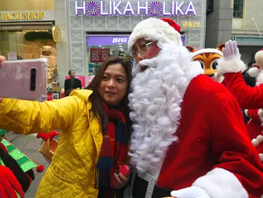 Seorang wanita berselfie dengan Santa Claus saat promosi musim Natal di distrik perbelanjaan di Seoul (13/11). Meski sebagian besar penduduknya adalah umat Budha, anak muda Korsel menikmati perayaan musim Natal tersebut. (AFP Photo/Jung Yeon-Je)