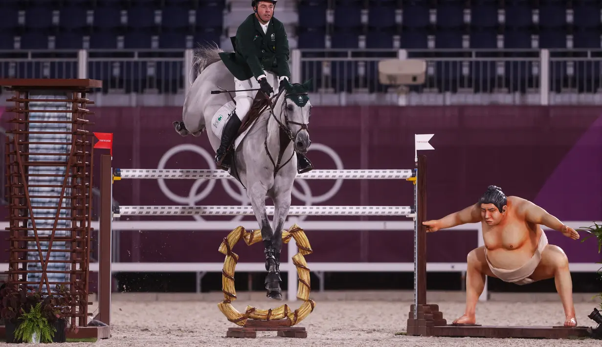 Cian O'Connor dari Irlandia mengendarai Kilkenny melewati patung pegulat sumo kecil di kualifikasi individu lompat berkuda selama Olimpiade Tokyo 2020 di Equestrian Park di Tokyo(3/8/2021). (AFP/Behrouz Mehri)