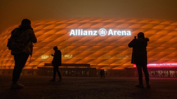 Orang-orang mengambil gambar Allianz Arena, markas FC Bayern Munchen, yang diterangi warna oranye untuk kampanye 