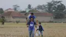 Seorang ayah menggendong anaknya saat melintasi sawah kering menuju Stadion Si Jalak Harupat, Bandung. (Bola.com/Vitalis Yogi Trisna)