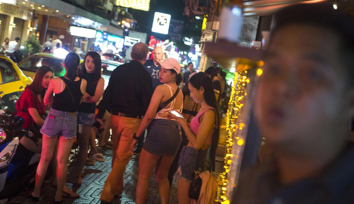 Foto pada 11 Oktober 2018 menunjukkan turis asing  berjalan melewati sekumpulan wanita di Nana Red Light Distrik, Bangkok, Thailand. Nana Red Light District memang dikenal sebagai kawasan hiburan malam terbesar di Bangkok. (Romeo GACAD / AFP)