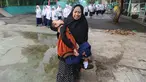 Fauzan Akmal Maulana (15), penderita Distrophia Muculor Progresive (DMP) atau penyakit otot lemah, digendong oleh ibunya, Winih Utami (49), saat bersekolah di SMP Terbuka 1 Tangerang Selatan, pada Jumat (22/3). (merdeka.com/Arie Basuki)