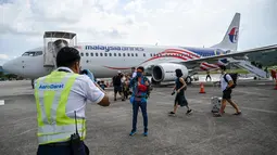 Petugas (kiri) membantu memotret penumpang setelah turun dari pesawat Boeing 738 Malaysia Airlines saat mendarat di Langkawi dari Bandara Internasional Kuala Lumpur (16/9/2021). Pulau liburan dibuka kembali untuk turis domestik setelah penutupan karena pembatasan Covid-19. (AFP/Mohd Rasfan)