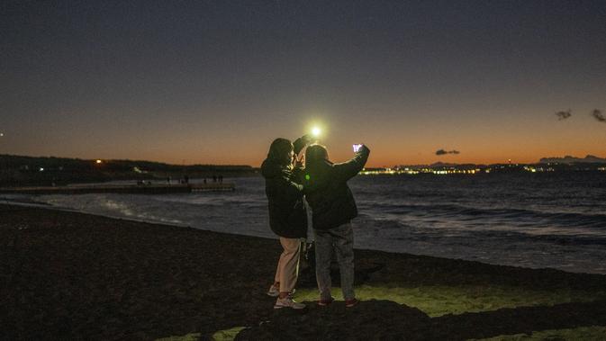 Dua wanita berfoto saat mereka menunggu matahari terbit di Pantai Selatan Chigasaki pada Hari Tahun Baru di Prefektur Kanagawa, barat daya Tokyo (1/1/2021). (AFP/Philip Fong)