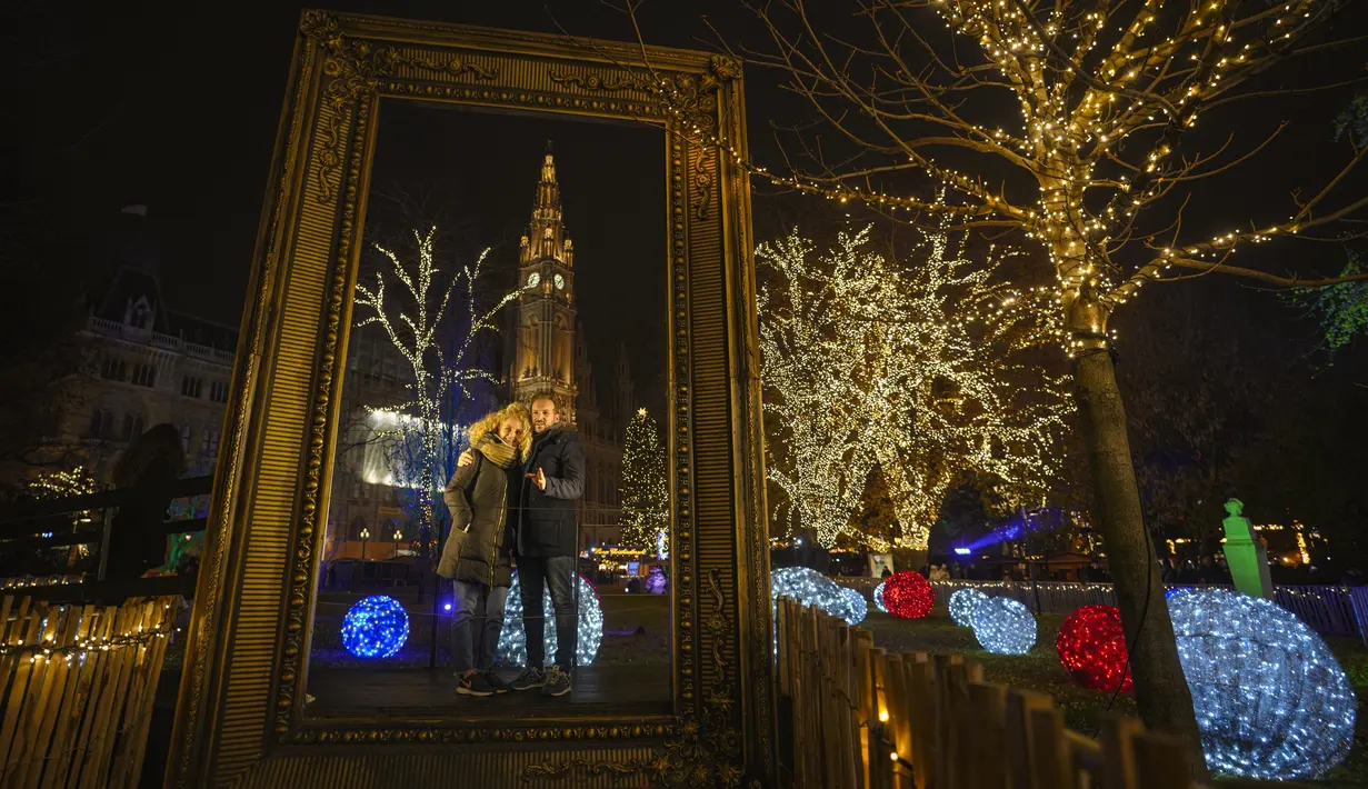 Sepasang kekasih berpose dengan latar belakang gedung balai kota di pasar Natal di Wina, Austria, Minggu (21/11/2021). Pemerintah Austria mengumumkan penguncian nasional yang akan dimulai Senin (22/11). (AP Photo/Vadim Ghirda)