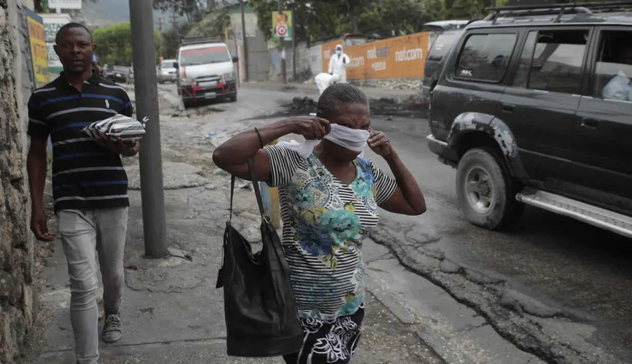 <p>Seorang wanita berjalan melewati pihak berwenang setempat yang memindahkan jenazah pria yang dibakar massa di Port-au-Prince, Haiti, Selasa (25/4/2023). (AP Photo/Odelyn Joseph)</p>