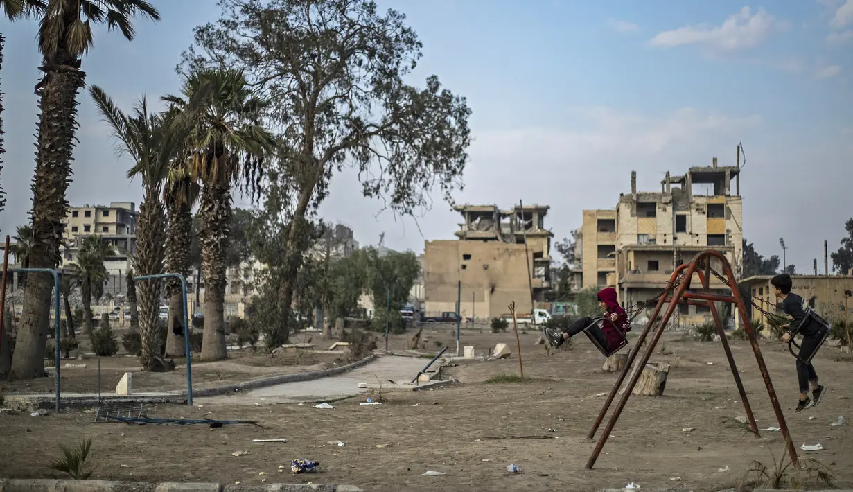 Anak laki-laki bermain ayunan di kota Raqqa, bekas ibu kota ISIS, di Suriah utara pada 20 Desember 2020. Raqqa menjadi saksi terusirnya anggota kelompok ekstremis oleh Pasukan Demokratik Suriah pada Oktober 2017 lalu. (Photo by Delil SOULEIMAN / AFP)