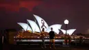 Anggota masyarakat berjalan melewati pita hitam yang melambangkan kenangan dan duka cita diproyeksikan ke Sydney Opera House pada 9 Februari 2023 sebagai bentuk solidaritas terhadap Turki dan Suriah setelah gempa bumi dahsyat meluluhlantakkan kedua negara tersebut. (DAVID GRAY/AFP)