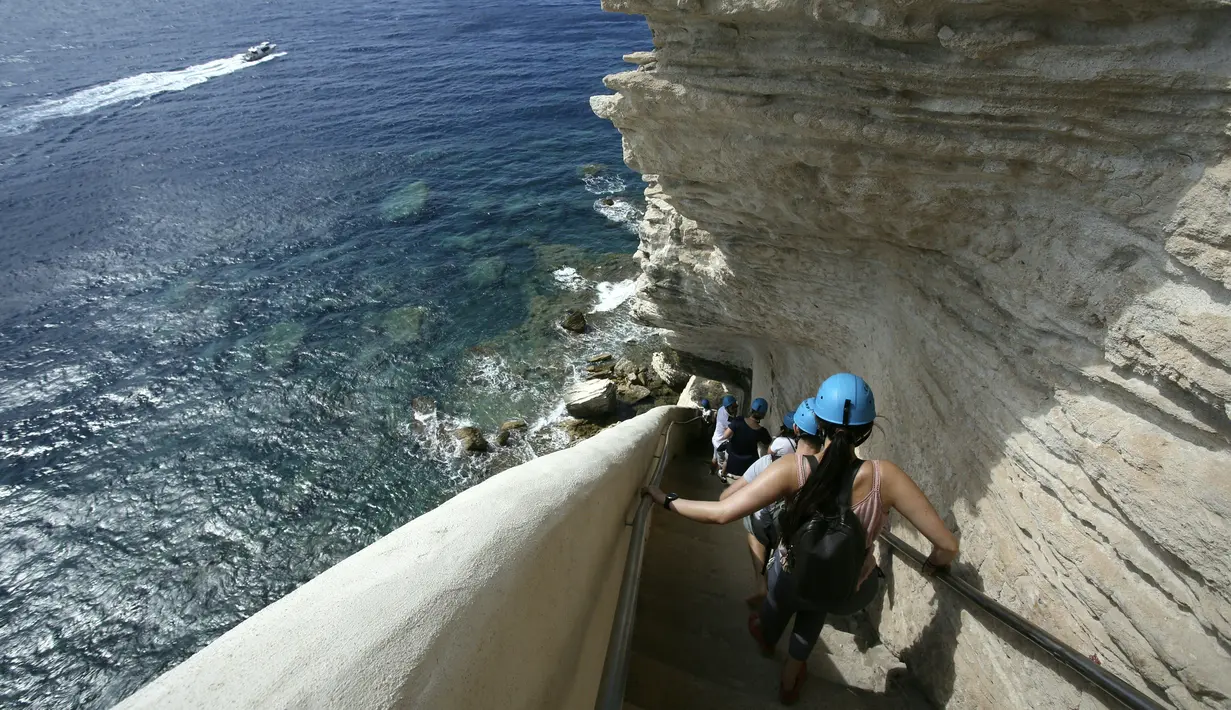 Turis menuruni tangga Raja Aragon di Bonifacio di pulau Corsica, Mediterania Prancis (19/9/2021). Pada kenyataannya, tangga itu digali oleh para biarawan Fransiskan untuk mengakses sumber air minum, yang tidak lagi digunakan. (AFP/Pascal Pochard-Casabianca)
