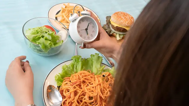 Seorang perempuan memegang jam weker sambil menatap makanannya (Foto Dok: Freepik/patty-photo)